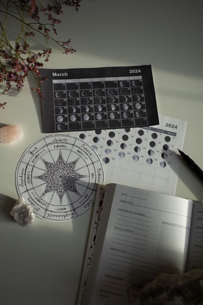 About A detailed view of astrology moon phases with a calendar and journal on a white desk.