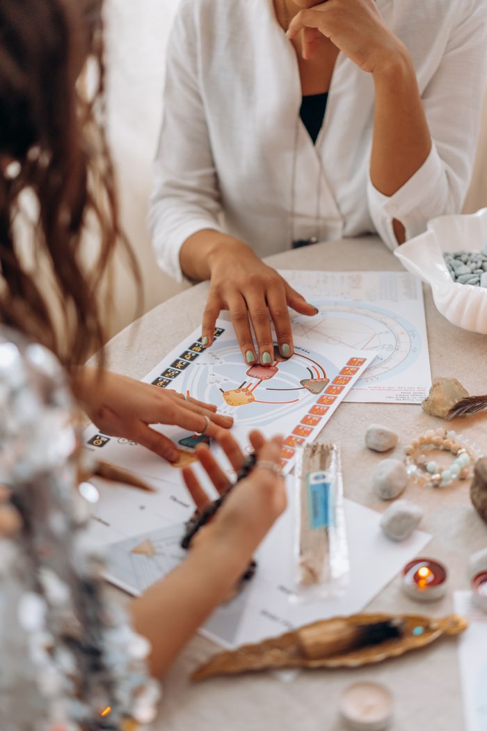 About Two women exploring astrology and tarot readings at a table with stones and candles.