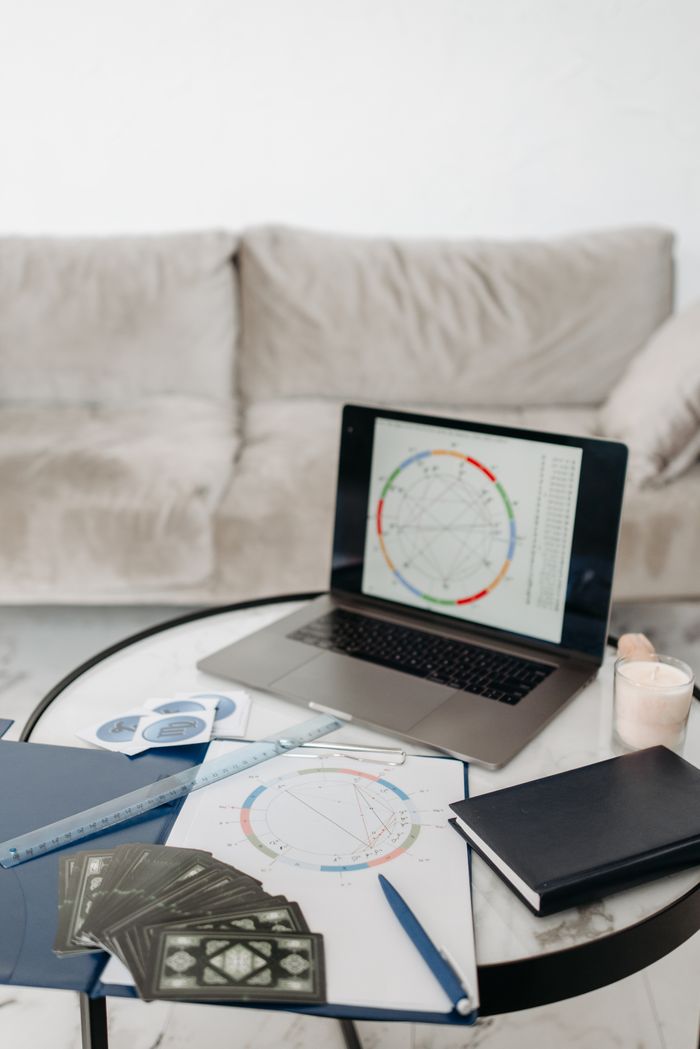 Services A cozy home office setup featuring a laptop with astrology chart, tarot cards, and a notebook on a table.
