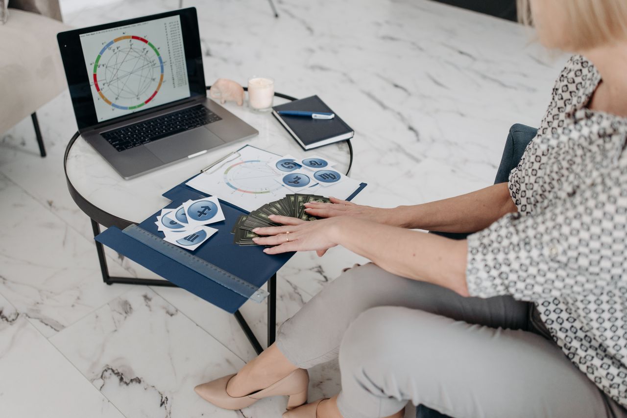 Services Astrology scene with a woman using a laptop and tarot cards in a modern living room.