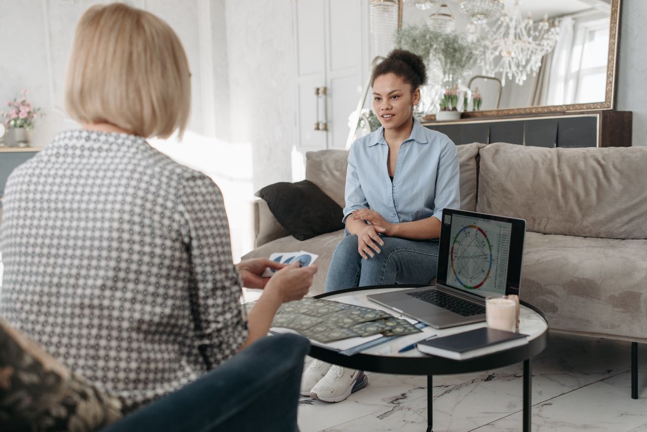 Services Women engaged in a tarot reading session with astrology charts on a laptop in a cozy living room.